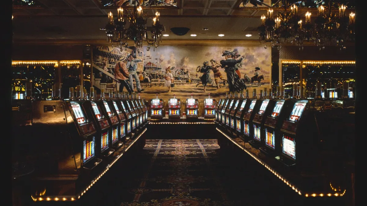 Two facing rows of lit slot machines under chandeliers on a dark casino floor